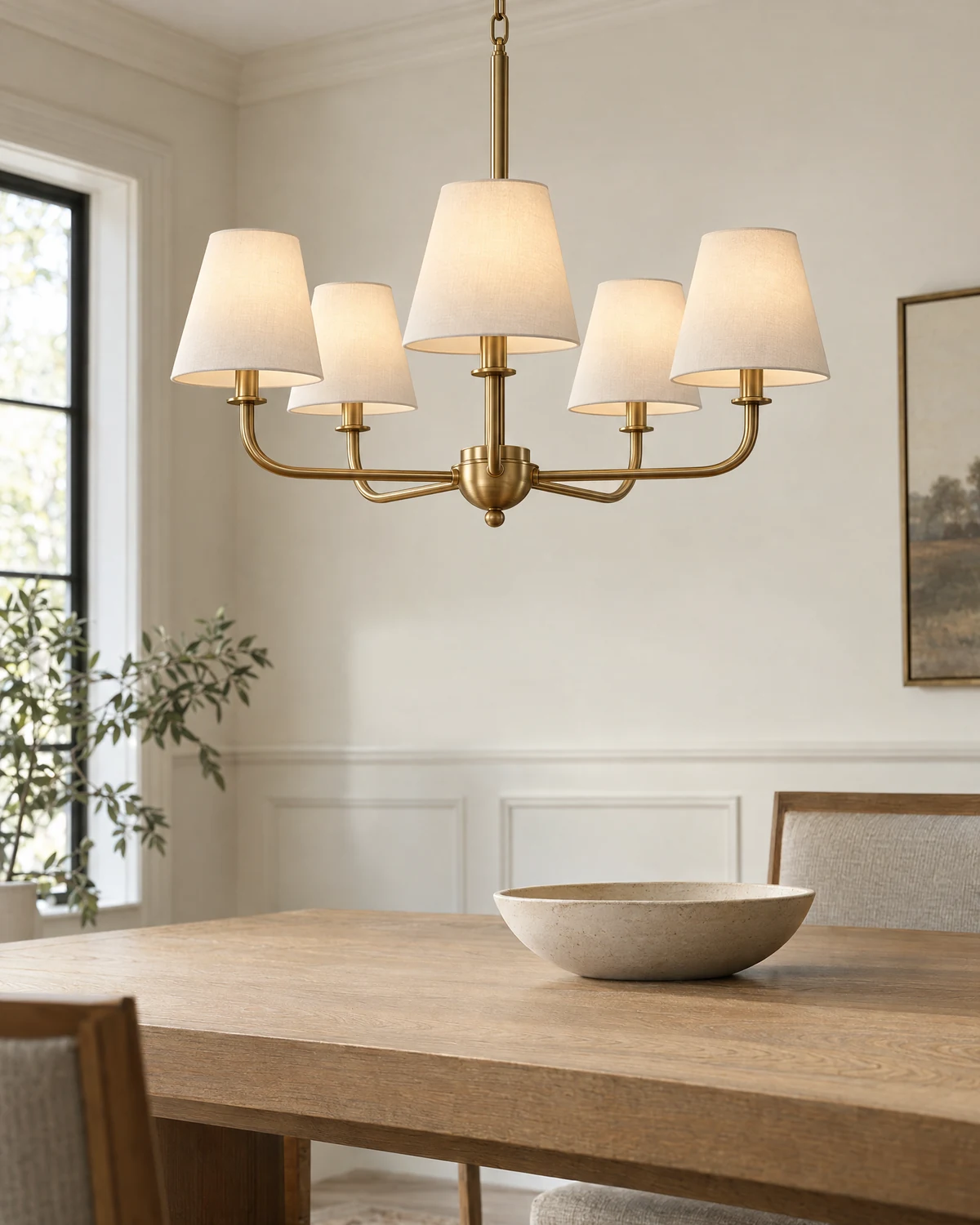 A restrained brass chandelier with linen shades above a natural oak dining table